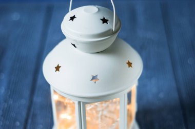 Beyaz, yanan mumları, ahşap masasında çam kozalakları ve arka planda parıltılı ışıkları olan klasik bir Fener. Noel arkaplanı. Mutlu yıllar. Seçici odak bütünlüğü.