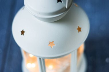 Beyaz, yanan mumları, ahşap masasında çam kozalakları ve arka planda parıltılı ışıkları olan klasik bir Fener. Noel arkaplanı. Mutlu yıllar. Seçici odak bütünlüğü.