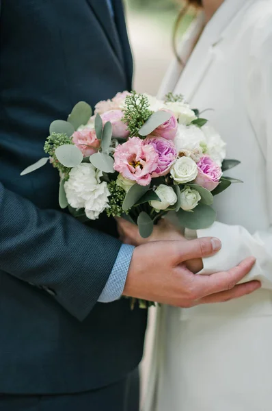 結婚式 スーツ姿の新郎と白いドレス姿の新婦が並んで白い花と緑の花束を持っています — ストック写真