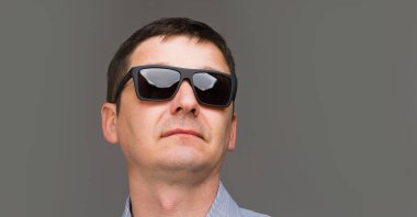 Gri arka planda gözlüklü bir adamın portresi.