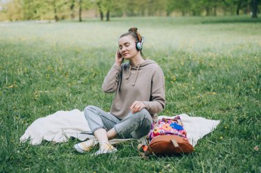 Güzel sarışın kız parkta çimlerde dinleniyor, kulaklıkla müzik dinliyor.