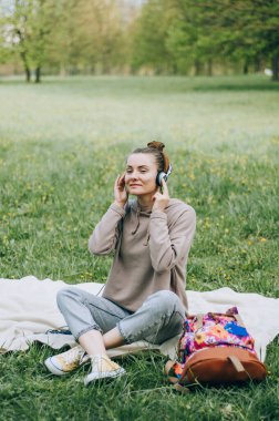 Güzel sarışın kız parkta çimlerde dinleniyor, kulaklıkla müzik dinliyor.