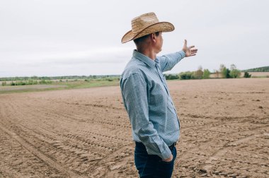 Kotlu ve gömlekli çiftçi adam saman işlerinden sonra tarlada duruyor, tablet de mesafeye bakıyor. Kırsal iş, tarım endüstrisi, işten sonra özgürlük, konsept
