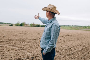 Kotlu ve gömlekli çiftçi adam saman işlerinden sonra tarlada duruyor, tablet de mesafeye bakıyor. Kırsal iş, tarım endüstrisi, işten sonra özgürlük, konsept