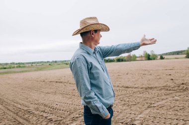 Kotlu ve gömlekli çiftçi adam saman işlerinden sonra tarlada duruyor, tablet de mesafeye bakıyor. Kırsal iş, tarım endüstrisi, işten sonra özgürlük, konsept