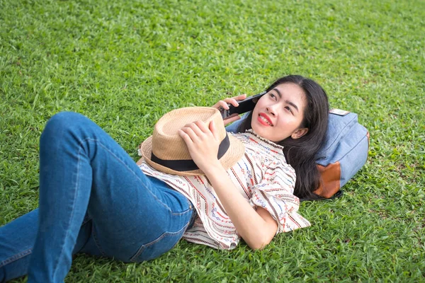 asian woman tourists backpacker are talking on the phone on the lawn at the public park and happy smile during travel the holidays and relax.