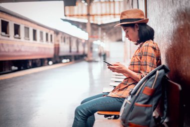 Asya genç kadın turistler turistik aramak ve seyahat haritasını görmek için akıllı telefon oynamak oturup. Hua Lamphong İstasyonu Bangkok Tayland at.