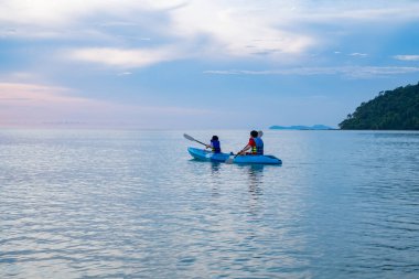 Gün batımında deniz manzarası. Gökyüzü bulutlarla dolu. Denizin ortasında kürek çeken genç erkekler ve kadınlar vardı..