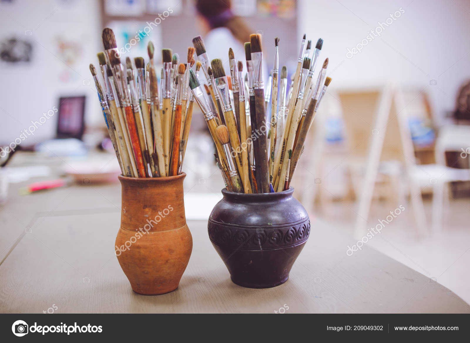 A Bunch Of Art Brushes Standing In Ceramic Vases On The Table In