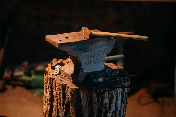 An old anvil attached to a wooden base stands in a private blacksmiths workshop.
