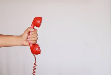 Eski bir kırmızı telefonu beyaz arka planda kızgın bir şekilde teslim etmek.