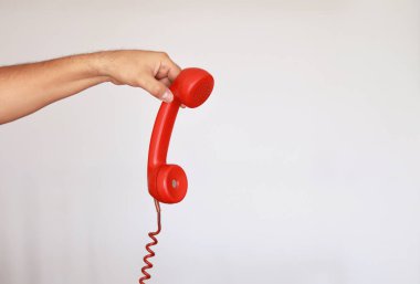 Eski model kırmızı bir telefonu parmaklarıyla beyaz arka planda tutuyordu.