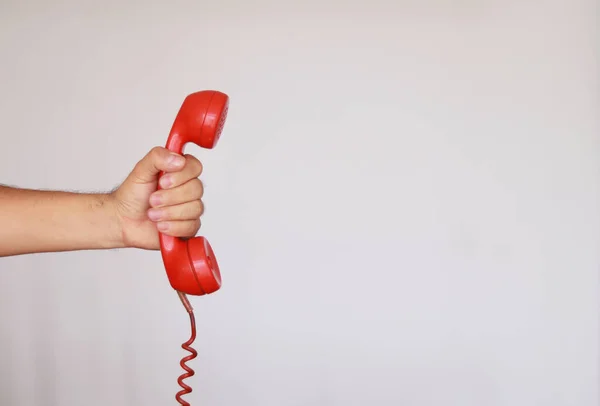 Eski bir kırmızı telefonu beyaz arka planda kızgın bir şekilde teslim etmek.