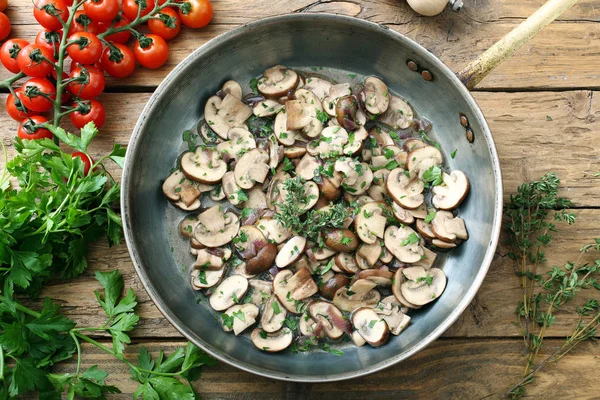 cooked mushrooms with herbs in metal pan on wooden table with tomatoes, top view