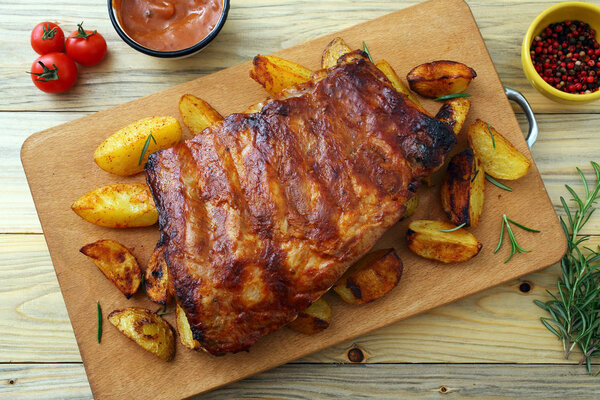 ribs pork BBq on chopping board with potato slices, spices and tomato sauce in bowls, top view