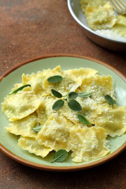 Vejetaryen ravioli tereyağı, adaçayı ve masa üzerinde metal kapta parmesan ile
