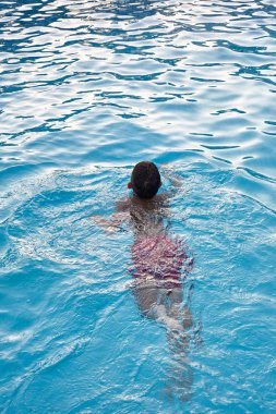 Çocuk bir havuzda yüzüyor.