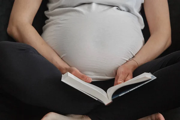 美しい妊婦がソファーに座って本を読んでいる — ストック写真