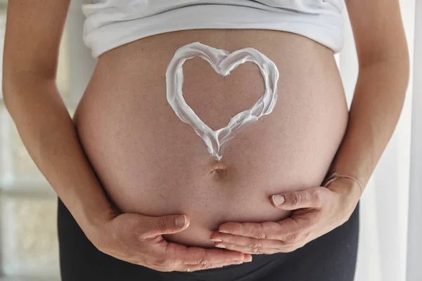 Heart painted with body cream on pregnant woman\'s belly.