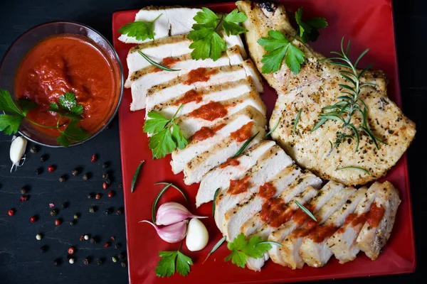 Pork steak with sauce and garlic on a red plate.