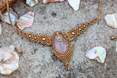 Doğal kayalık ve odunsu arka planda değerli taşlı Macrame kolye