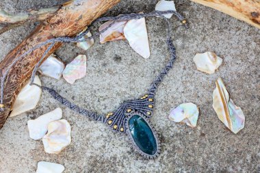 Doğal kayalık ve odunsu arka planda değerli taşlı Macrame kolye