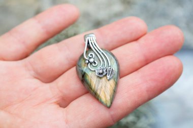 Kadın eli üzerinde gümüş süsler olan labradorit kolye.