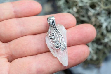 Doğal kristal kuvars taşı. Kadın elinde gümüş süsleme kolyesi var.