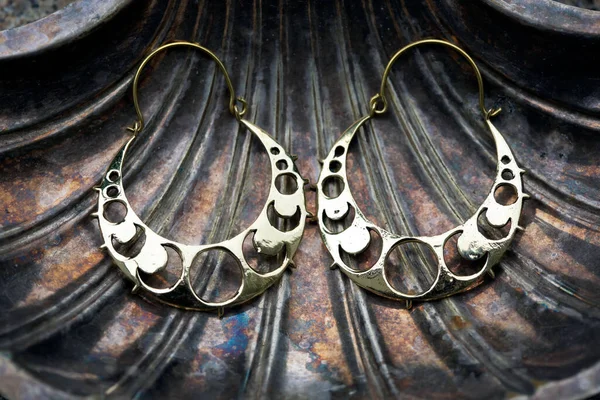 Brass metal earrings in the shape of moon phases on decorative silver shell background