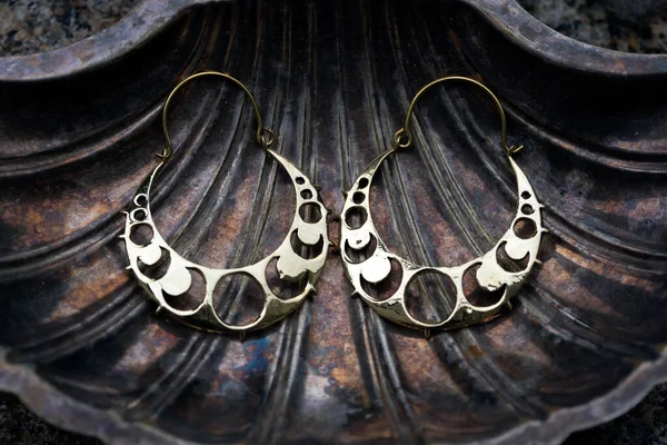 Brass metal earrings in the shape of moon phases on decorative silver shell background