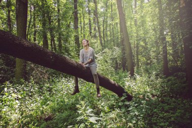 Genç bir kadın ağaçta oturuyor ve çevresindeki doğanın tadını çıkarıyor.