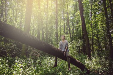 Genç bir kadın ağaçta oturuyor ve çevresindeki doğanın tadını çıkarıyor.