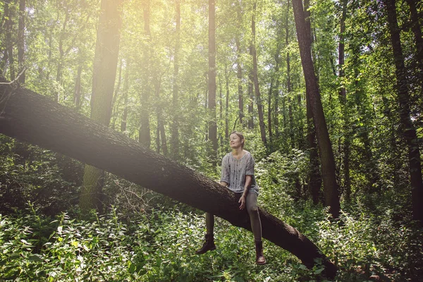Genç bir kadın ağaçta oturuyor ve çevresindeki doğanın tadını çıkarıyor.