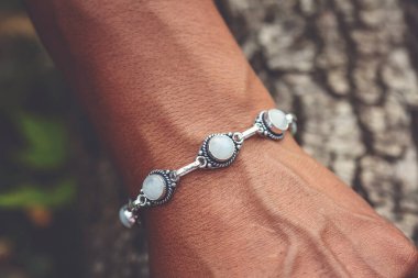 Açık havada bir el bileğinin yakın çekimi. Üzerinde ay taşı değerli gümüş bir bilezik var.