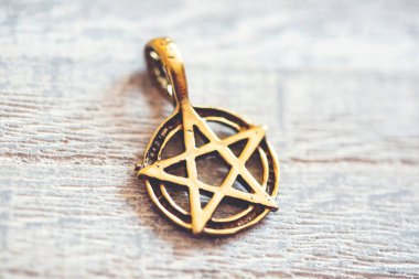 Tahta arka planda altın renginde pentagram kolye.