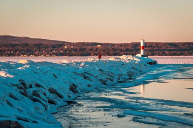 Gün batımında Petoskey Michigan 'da donmuş bir deniz fenerini ziyaret eden bir turist.