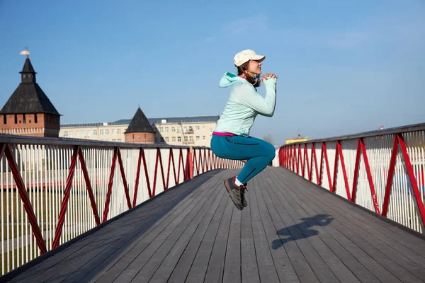 woman jumping on a wooden bridge, cardio exercise outdoors, taking care of her body, staying healthy and fit, in a white baseball hat, motion