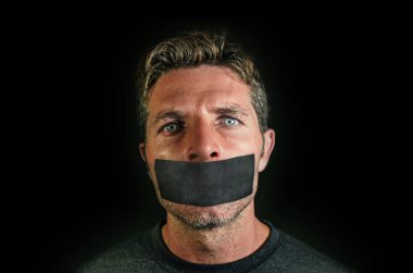 young man with mouth and lips sealed covered with adhesive tape in censorship coerced freedom of speech and forced silence and secrecy concept isolated on dark black background clipart