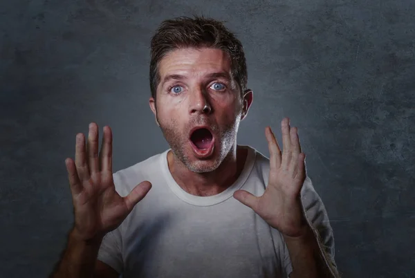 portrait of young attractive Caucasian man in shock and surprised rising hands amazed and alarmed with mouth and eyes wide open in disbelief and surprise face expression isolated on grey background