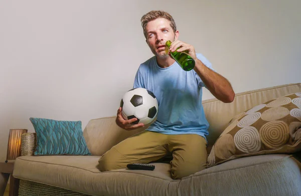 young attractive and nervous man concentrated watching football game on television holding beer bottle and soccer ball excited in stress enjoying the match on sofa couch in supporter concept