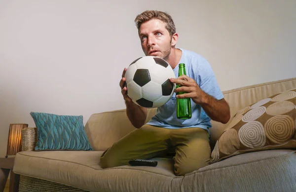 young attractive and nervous man concentrated watching football game on television holding beer bottle and soccer ball excited in stress enjoying the match on sofa couch in supporter concept