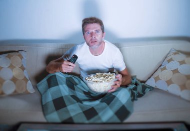 oturma odası koltuk kanepe zevk tamamen konsantre ve baktılar, gece geç saatlerde oturan patlamış mısır yemek televizyon film izlerken genç çekici rahat bir adam portresi yaşam tarzı
