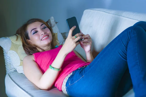 young gorgeous and happy hispanic woman lying on home sofa couch using internet app on mobile phone sending text relaxed and smiling cheerful in communication lifestyle concept