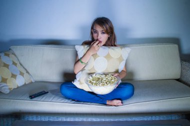Genç güzel latin kadın tamamen evde oturan koltuk kanepe geç gece kız aile içi yaşam tarzı kavram çok ilgi patlamış mısır yemek geceleri yoğun film izlerken konsantre