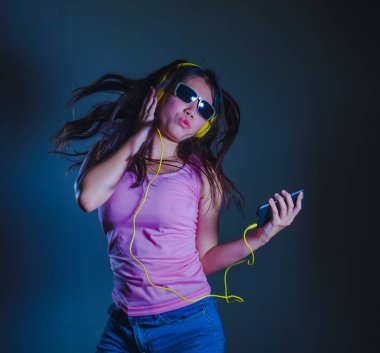 dans ve cep telefonu karanlık studio arka plan üzerinde izole eğleniyor tutan sarı kulaklık ile müzik şarkı için şarkı genç mutlu ve çekici Asyalı Koreli kadın