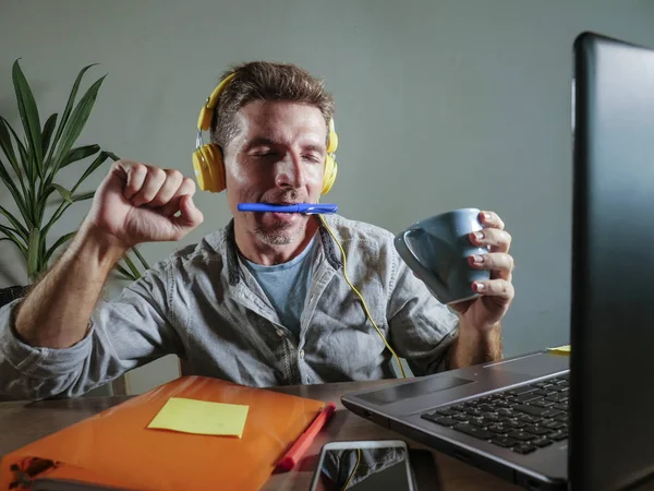 young attractive and happy man with yellow headphones sitting at home office desk working with laptop computer having fun listening to music enjoying song excited in lifestyle concept