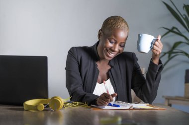 genç çekici ve mutlu başarılı siyah afro Amerikalı kadın iş ceket çalışma neşeli ofis dizüstü içme çay gülümseyen iş başarı kavramı memnun Not almak