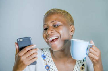 çay ya da kahve fincan neşeli ve iletişim yaşam tarzı heyecan cep telefonu gülümseyen internet sosyal medya app kullanarak tutan izole genç çekici ve mutlu siyah afro Amerikan kadın
