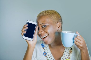 çay ya da kahve fincan neşeli ve iletişim yaşam tarzı heyecan cep telefonu gülümseyen internet sosyal medya app kullanarak tutan izole genç çekici ve mutlu siyah afro Amerikan kadın