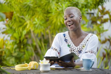 Genç mutlu ve çekici siyah afro Amerikan hipster kadın dijital tablet ile açık havada kafe rahat ve neşeli dijital göçebe başarılı seyahat ve yaşam tarzı blogger serbest iş içinde çalışan.
